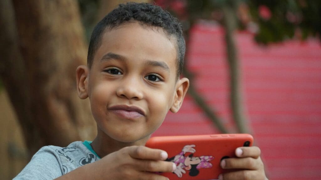 Image shows a smiling boy holding a red mobile phone.