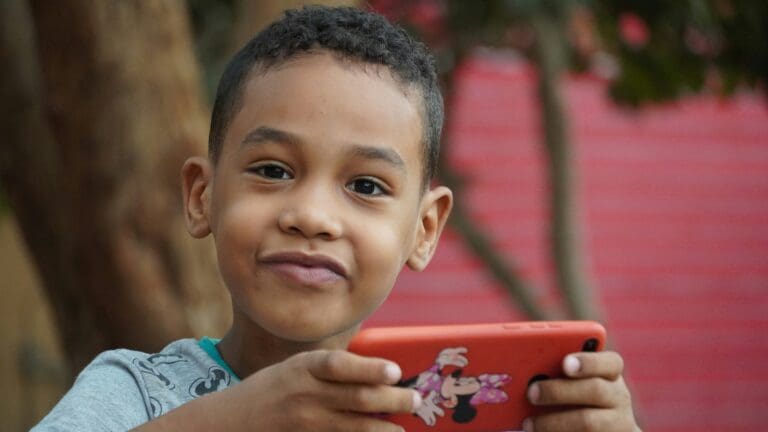 Image shows a smiling boy holding a red mobile phone.